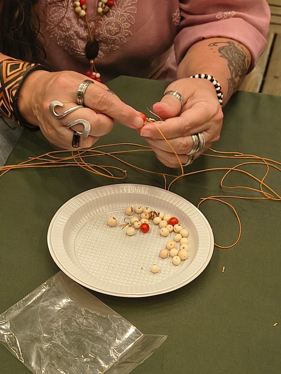 Detalhe das mãos enfiando sementes de juçara no fio para fazer colar